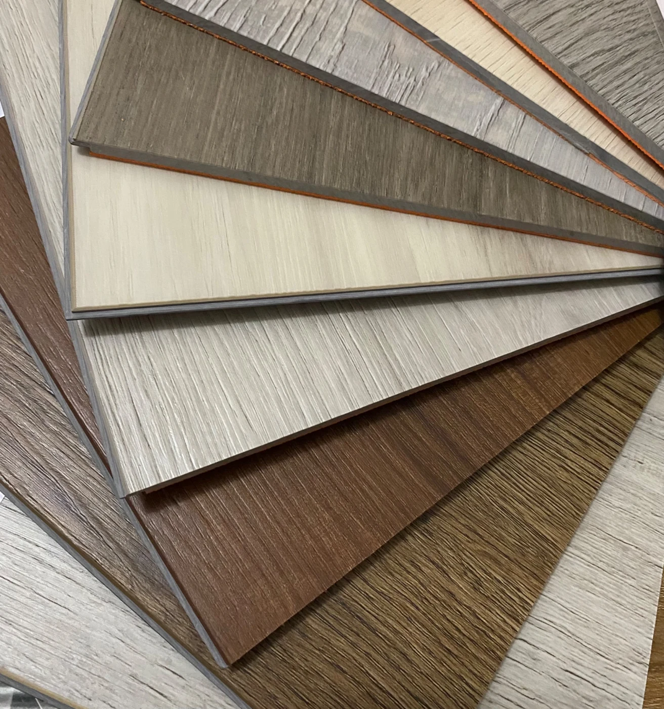 Overlapping LVT flooring samples in light, gray, and warm brown wood tones.